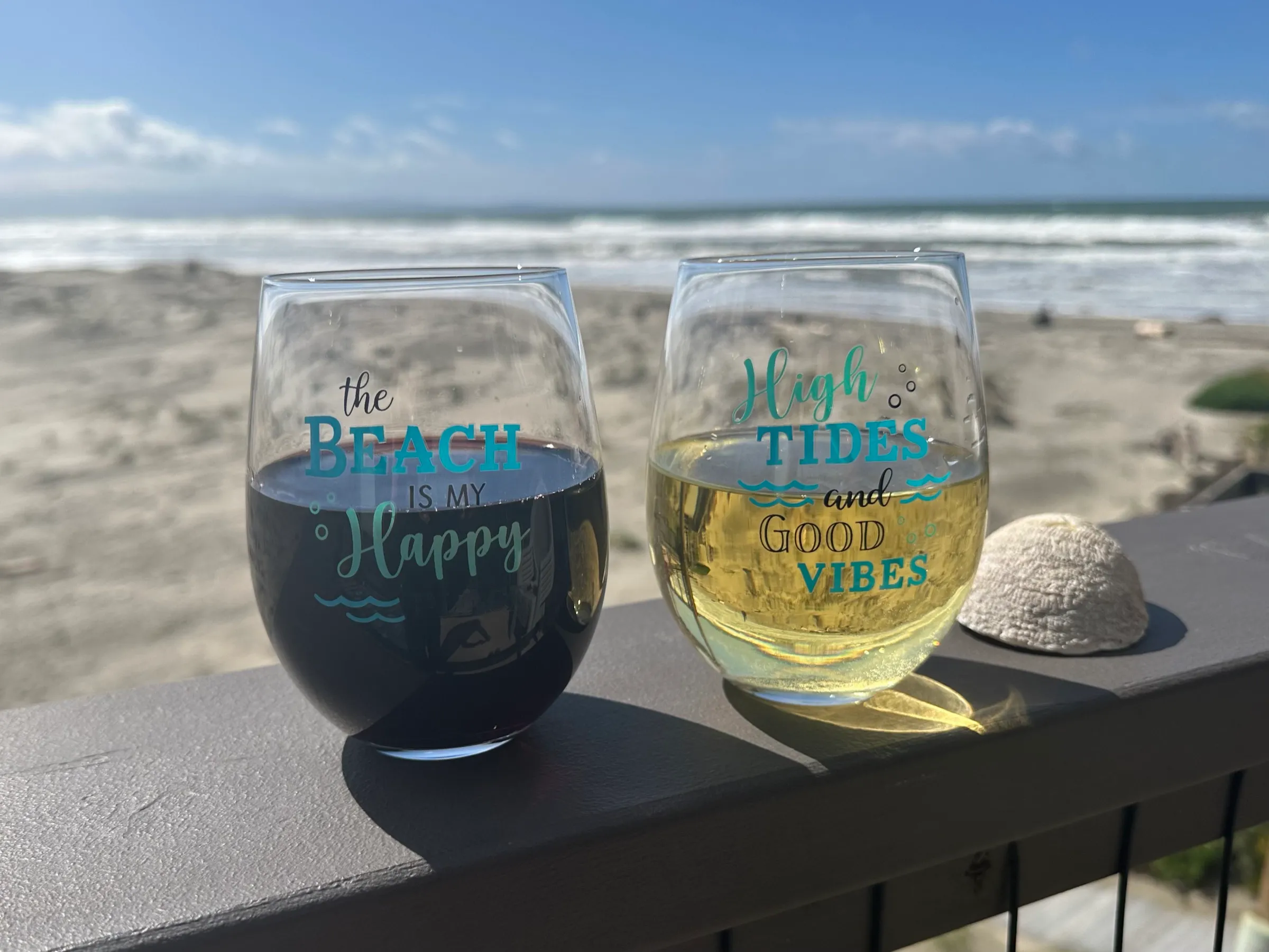 Two wine glasses on the balcony rail, with the beach beyond