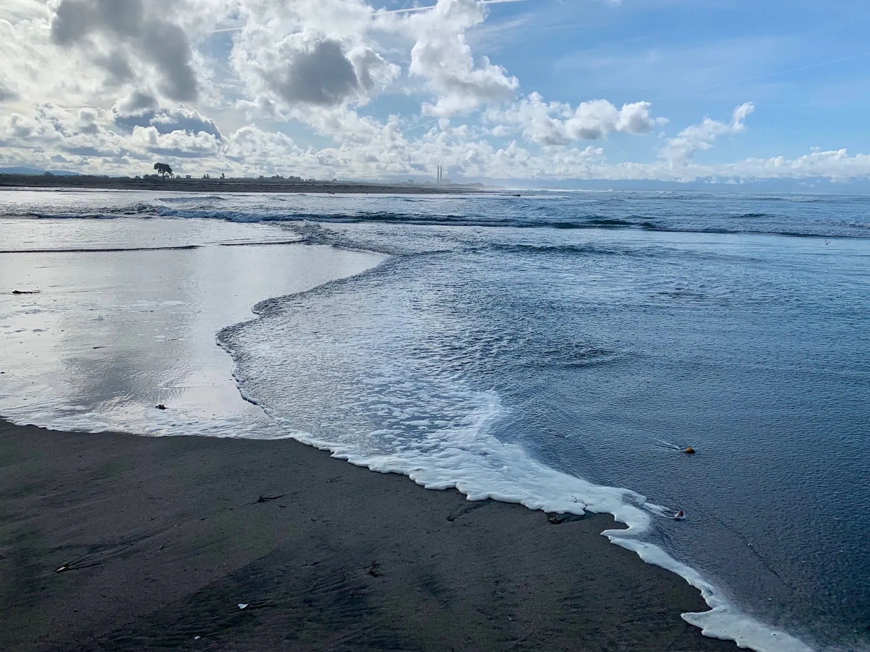 A wave washing up the wet sand under a cloudy sky